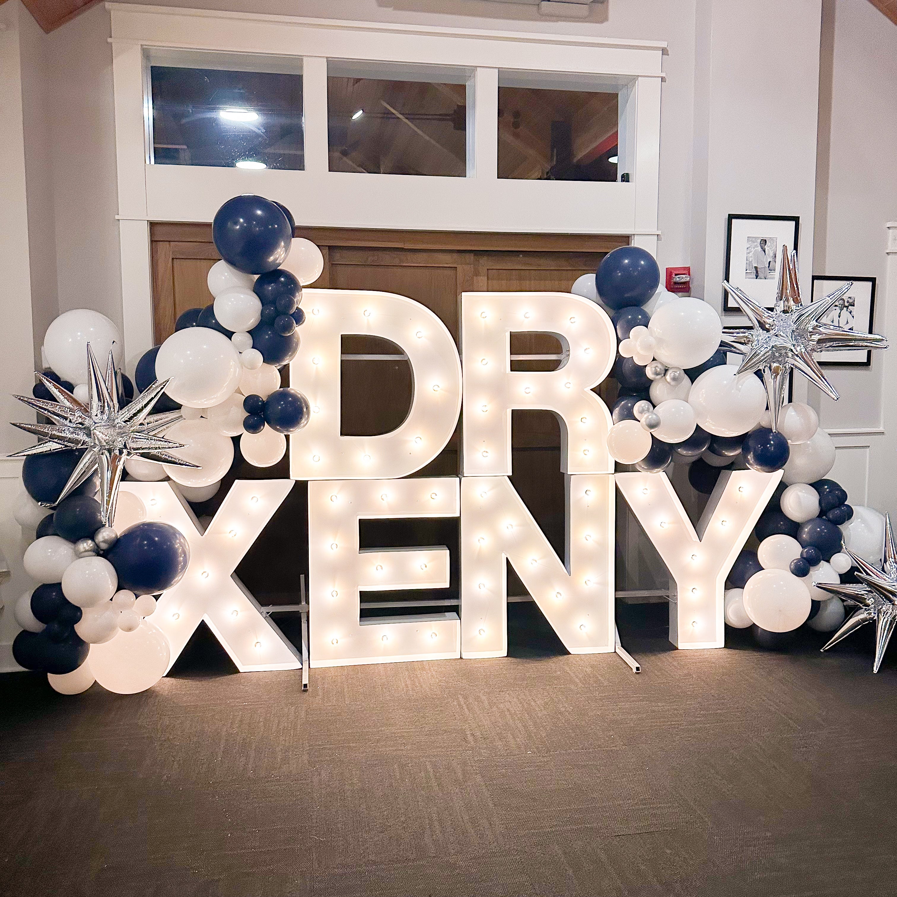 marquee letters that read Dr Xeny. There are balloons in navy and white with silver starbursts around the marquee letters. The marquee letters are lit.