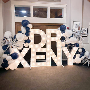 marquee letters that read Dr Xeny. There are balloons in navy and white with silver starbursts around the marquee letters.  The marquee letters are lit.