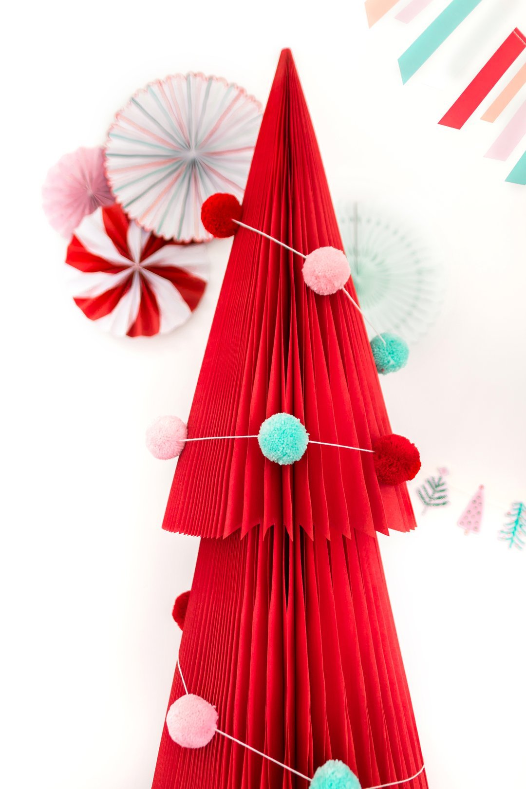 Festive holiday pom pom garland wrapped around a red paper Christmas tree decoration
