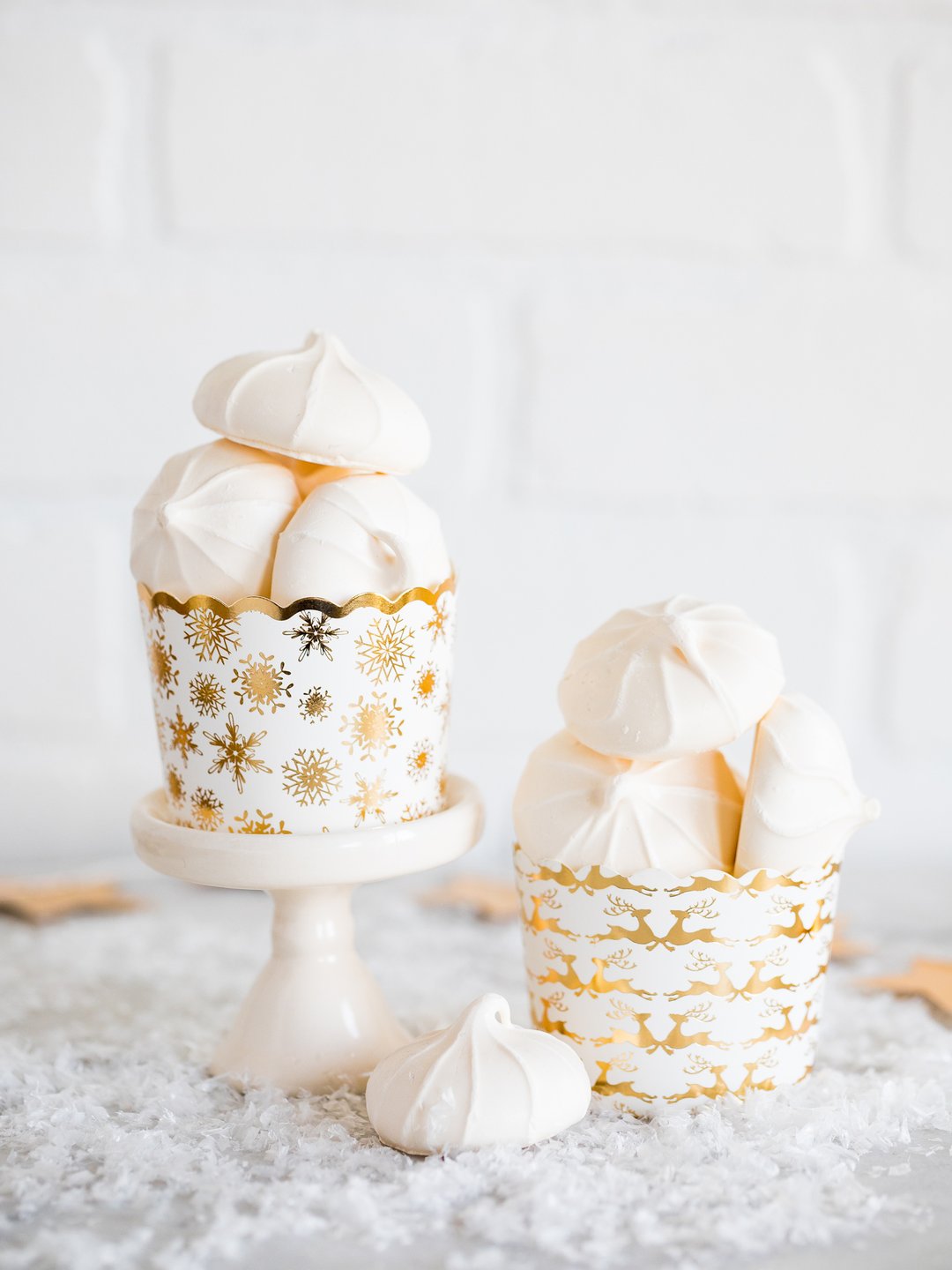 A gold foil and reindeer festive baking cup on a small cupcake plate with festive baked goods inside one a snow sprinkled table