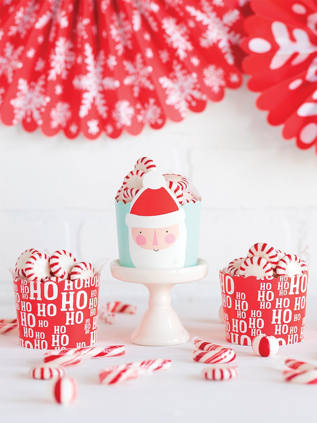 Ho Ho Ho Santa Baking cups displayed on a table with candy canes spread around them and each cup holding red and white mint candies