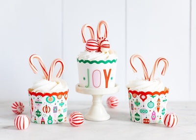 Joy baking cups displayed against a white backdrop and filled with cupcakes surrounded by red and white mint candies.
