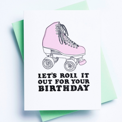 A white birthday card with an image of a roller skate and the words 'let's roll it out for your birthday' displayed over a green envelope and white background