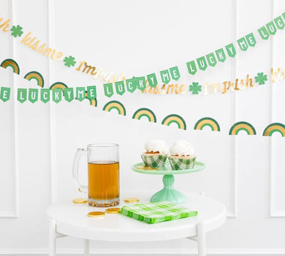 St. Patrick's Day themed banners displayed against a white wall with a small table in front containing other St. Patrick's themed goodies and party supplies