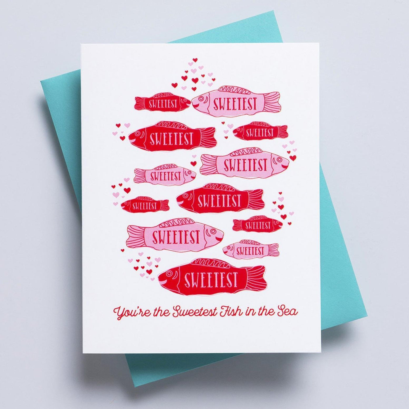 A white valentines greeting card with images of 'sweetest fish' in red a pink on the face of the card and the text 'you're the sweetest fish in the sea' written on the bottom. 