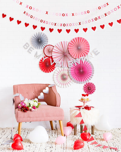 Valentines day party fans displayed in front of a white wall with other valentine's day decorations