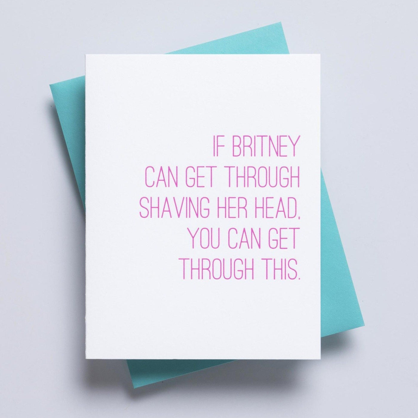 A simple white greeting card accompanied by a blue envelope and pink text on the face of the card reading 'if britney can get through shaving her head, you can get through this'. 